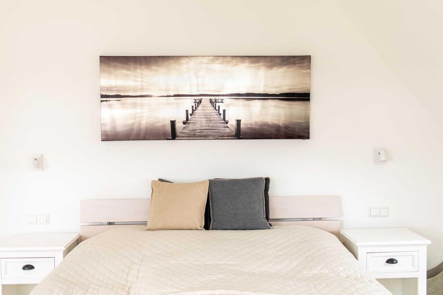 A bedroom with a bed, two nightstands, and a wall-mounted picture of a pier extending into a body of water.