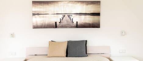 A bedroom with a bed, two nightstands, and a wall-mounted picture of a pier extending into a body of water.
