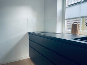 Una cocina moderna con encimera oscura, salpicadero de vidrio transparente y ventana con persianas.