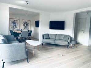Un salon moderne avec un canapé gris, une petite table blanche et un coin repas comprenant des chaises et une table.