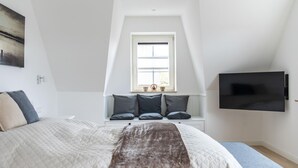 A bedroom with a large bed, a window with a view, a mounted TV, and a small bench.
