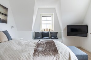 Un dormitorio con una cama grande, una ventana con vistas, un televisor montado y un pequeño banco.