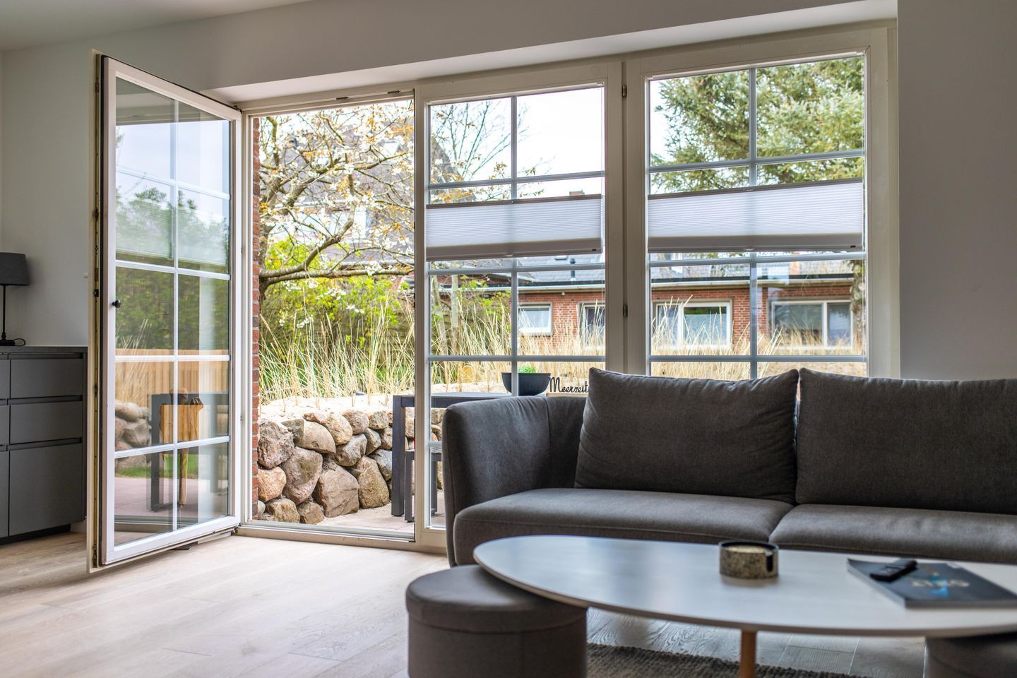Ein modernes Wohnzimmer mit grauem Sofa, einem runden Couchtisch und einer Glastür, die auf eine Terrasse führt.