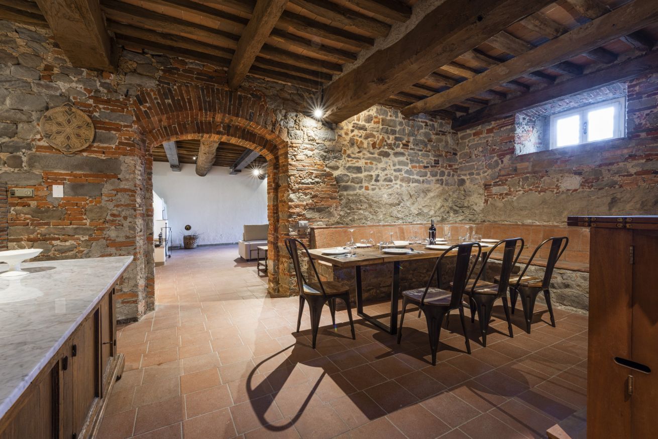 Une cuisine rustique en pierre, avec un coin repas, des poutres en bois et une arche en pierre.