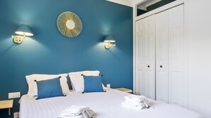 A neatly made bed with white linens and blue pillows, two wall-mounted lamps, and a white wardrobe. - Villa de la Côte - Welkeys (Labenne)