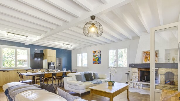 A spacious living area with a white sofa, a dining table, and a fireplace. - Villa de la Côte - Welkeys (Labenne)
