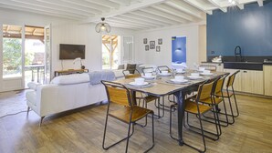 A modern kitchen with white cabinetry, a dining area with a wooden table and chairs, and a large window providing natural light. - Villa de la Côte - Welkeys (Labenne)
