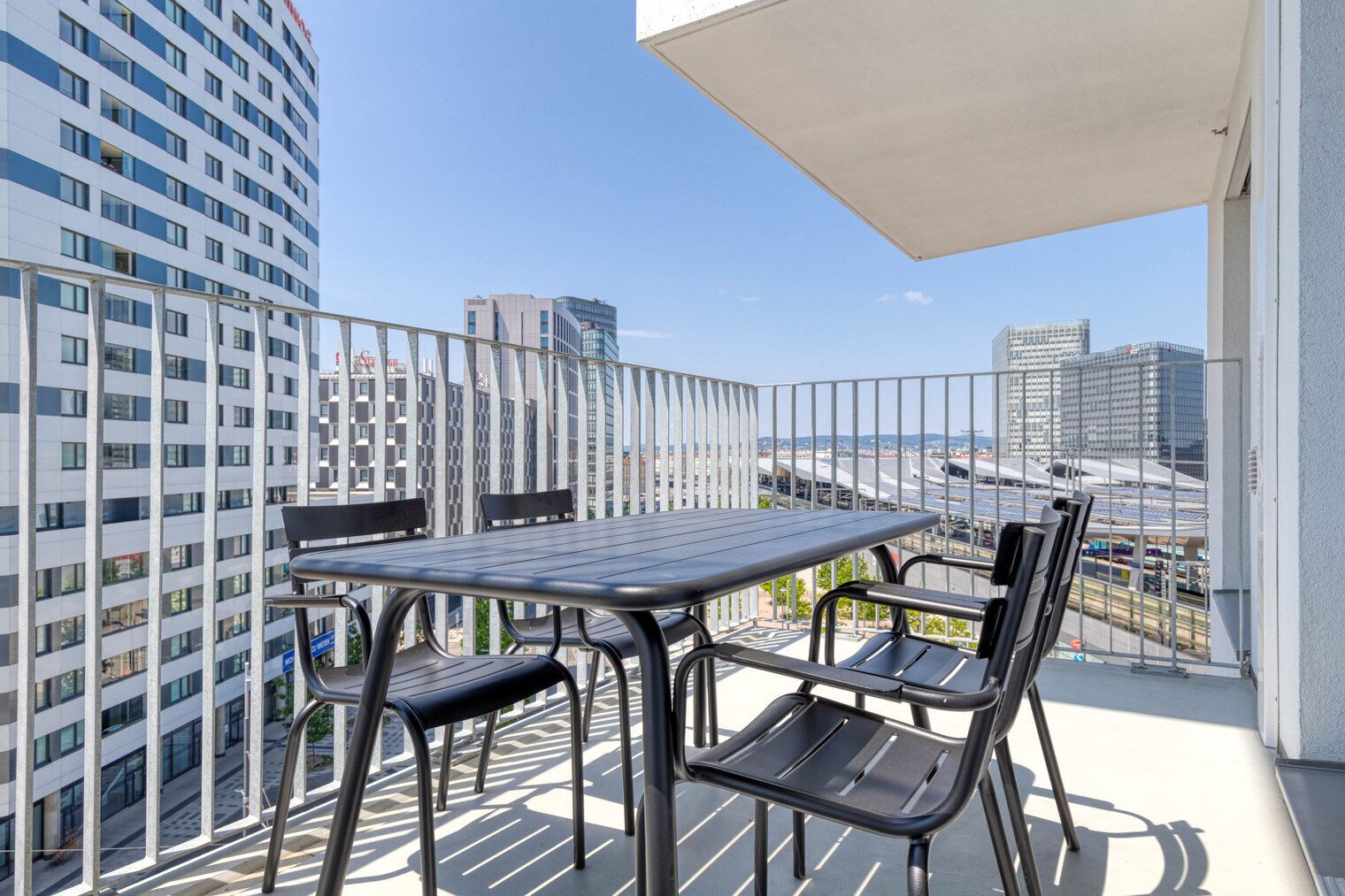 Ein Balkon mit Tisch und Stühlen, mit Blick auf eine Skyline moderner Gebäude.