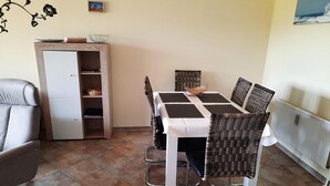 Un coin repas avec une table dressée pour quatre personnes, entouré de chaises en osier, d’un canapé et d’un meuble avec une porte.