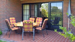 Une terrasse avec un sol en briques, une table entourée de chaises et une porte-fenêtre coulissante donnant sur un jardin.