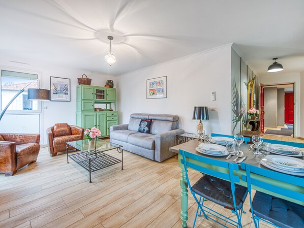 A living room with a sofa, armchairs, a coffee table, and a dining area with a table set for four. - Appartement Thiers - Welkeys (Antibes)