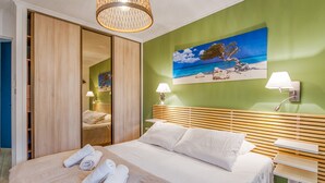 A hotel room with a bed, a mirror, a painting of a beach, and a wooden headboard. - Appartement Thiers - Welkeys (Antibes)