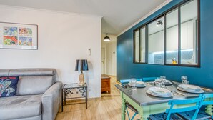 A modern living room with a grey sofa, a small table with a lamp, and a dining area with a blue table and chairs. - Appartement Thiers - Welkeys (Antibes)