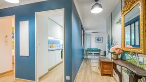 A hallway with blue walls, wooden flooring, a dining area with a table and chairs, and a large ornate mirror. - Appartement Thiers - Welkeys (Antibes)