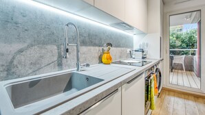 A modern kitchen with a large sink, a yellow vase, and a view of a balcony. - Appartement Thiers - Welkeys (Antibes)