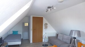 A modern, well-lit attic bedroom with a sloped ceiling, a bed, a sofa, a lamp, and a small table. - Vacation apartment Am Harlebogen 11 Whg. 4 (Wittmund)