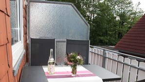 A balcony with a table set for two, a bottle of white wine, and a vase with flowers. - Vacation apartment Am Harlebogen 11 Whg. 4 (Wittmund)