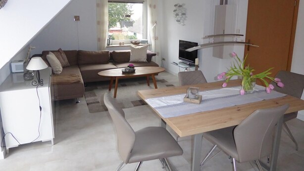A modern living room with a sofa, coffee table, and dining area. - Vacation apartment Am Harlebogen 11 Whg. 4 (Wittmund)