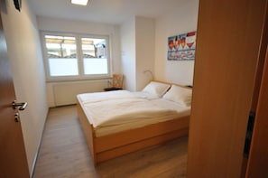 A bedroom with a wooden bed, a chair, a window, and a painting on the wall.