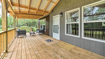 A covered deck with wooden flooring, two wicker chairs, a small table, and a door.