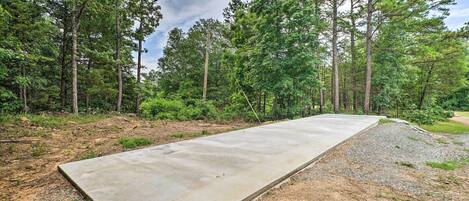 A concrete pathway in a forested area with tall trees and a gravel path on one side.