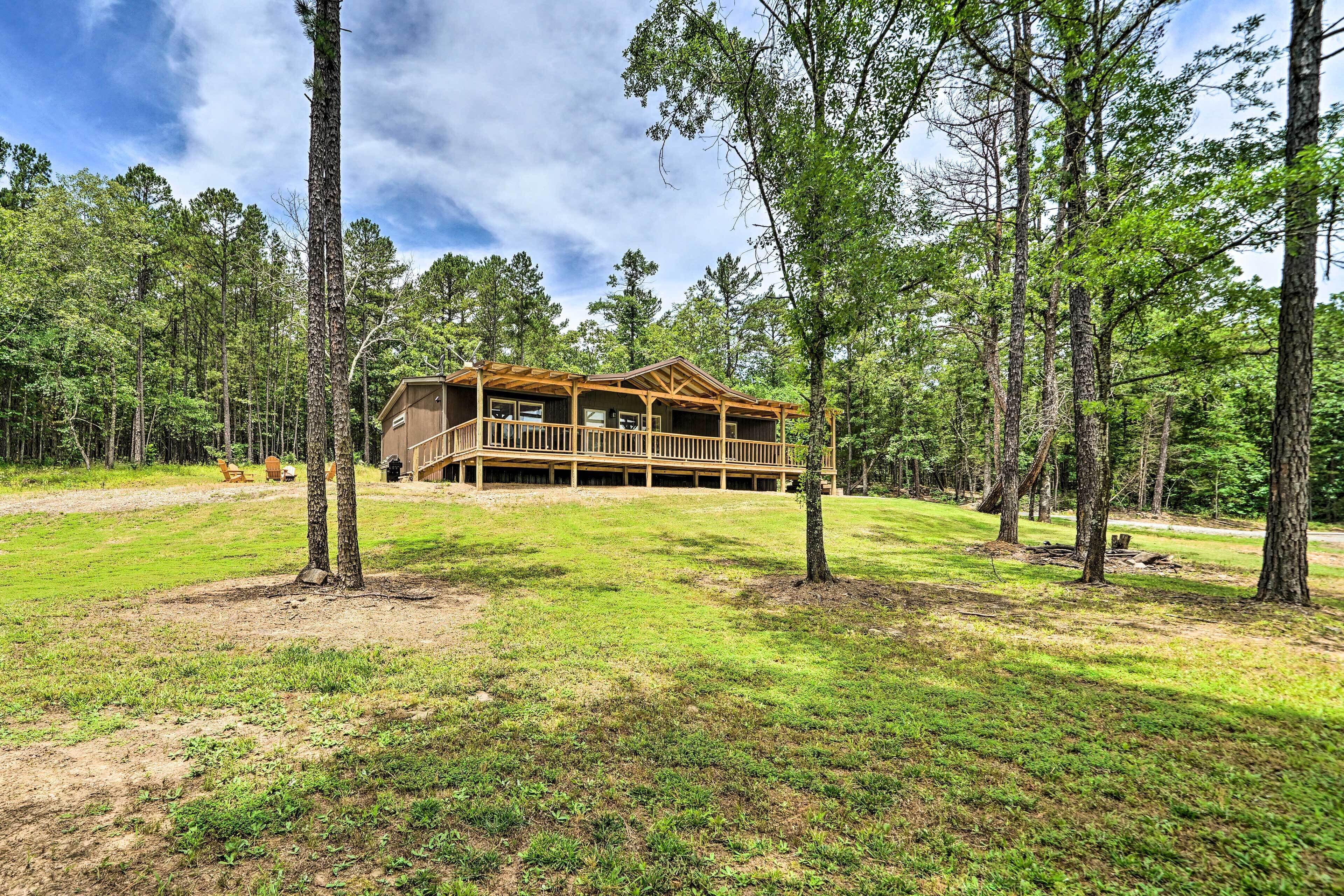 A cabin with a porch, surrounded by trees and grassy area.