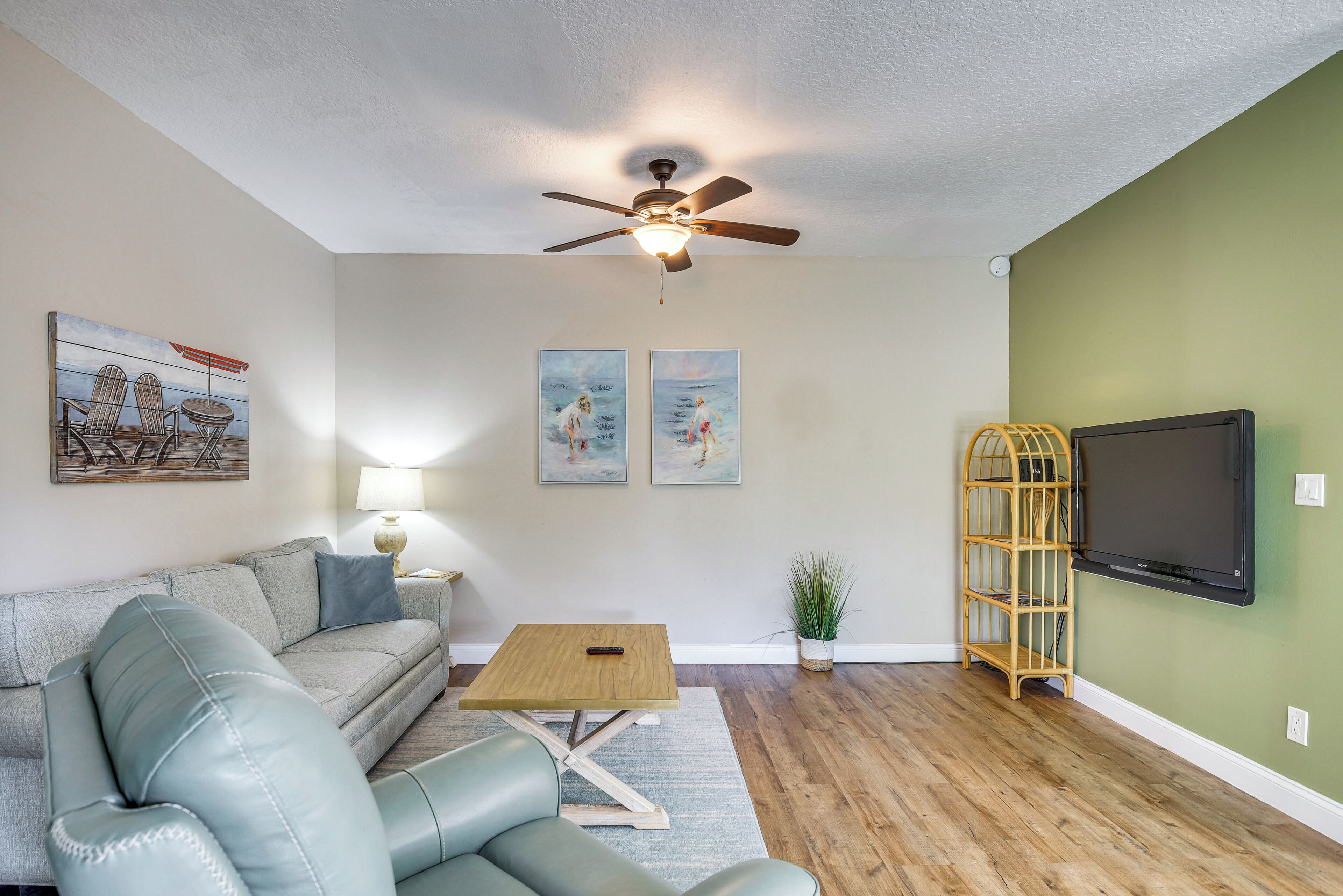A living room with a ceiling fan, a flat-screen TV, a wooden coffee table, a sofa, and two paintings on the wall.