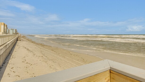 Ein Strand mit einer Betonpromenade und Gebäuden im Hintergrund.