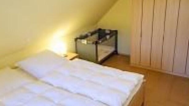 A small, single-room with a bed, a nightstand, and a wooden wardrobe. - Vacation home Wittmunder Str. 37 F (Wittmund)
