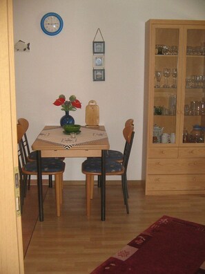 A dining area with a wooden table, two chairs, a vase with flowers, a clock, and a cabinet with glass doors. - Vacation Apartment at Am Harlebogen 10, Apt. 2 (Wittmund)