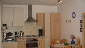 Una cuina compacta amb electrodomèstics bàsics, armaris de fusta i zona de menjador amb taula i cadires.