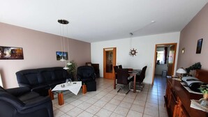 Una sala de estar con un sofá, una mesa de comedor y sillas. Hay una puerta que da a otra habitación.