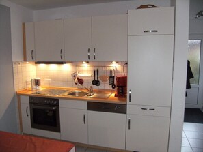 A compact kitchen with white cabinets, a stainless steel sink, a coffee maker, and a dishwasher. - Apartment Jonathan Whg. 5 - Apartment Tulpenweg 4 Jonathan Whg. 5 (Neuharlingersiel)