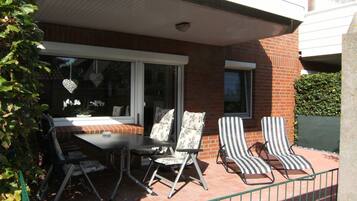 Eine Terrasse mit Tisch und zwei gestreiften Stühlen, ein Fenster mit Dekoration und ein Backsteinhaus im Hintergrund.