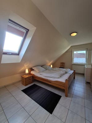 Une chambre avec un plafond en pente, un puits de lumière, un lit avec des oreillers et une couverture, une table de chevet avec une lampe et un radiateur.