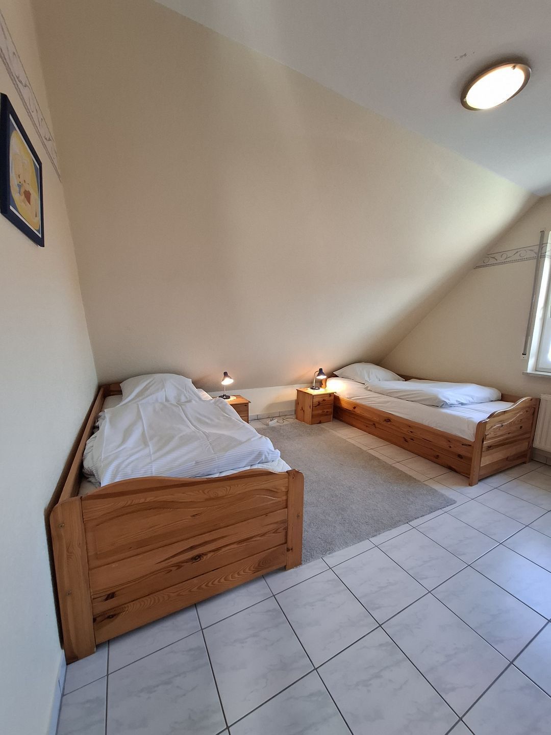 Un dormitorio con dos camas de madera, una ventana pequeña y una lámpara en el techo.