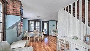 Una habitación amplia con piso de madera, una mesa de comedor con sillas, un escritorio blanco y una escalera con barandales de madera.