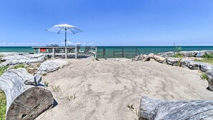 Una playa con un muelle de madera, una sombrilla blanca y vista al océano.