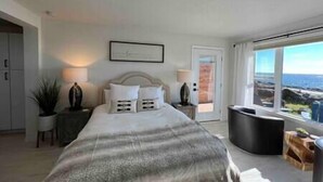 Een slaapkamer met een groot bed, een nachtkastje, een stoel en uitzicht op de omgeving door een raam.
