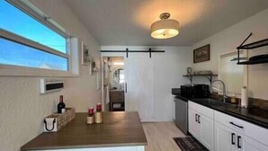 Een kleine keuken met witte kastjes, een houten aanrecht en een hangende lamp.