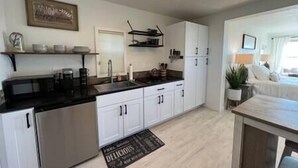 Een moderne keuken met witte kastjes, een roestvrijstalen koelkast en een zwart aanrecht. Er is een klein eiland met een spoelbak en een ophangrek erboven.
