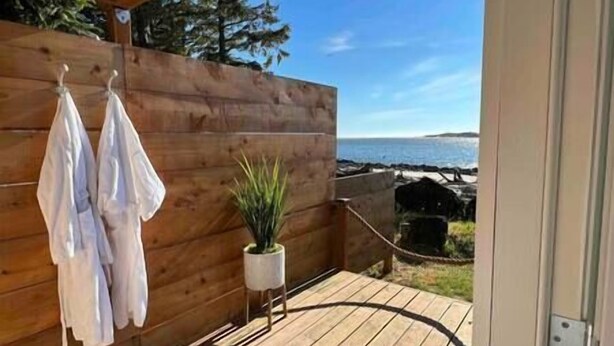 Een houten terras met uitzicht op de oceaan, een bloempot en twee witte handdoeken hangen aan een houten muur.