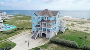 Une propriété en bord de mer, composée de plusieurs étages, dotée d’une piscine, de nombreux balcons et d’un escalier menant à l’entrée principale.