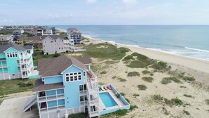 Une propriété située sur la côte, avec une grande maison bleue dotée d’une piscine et de plusieurs balcons.
