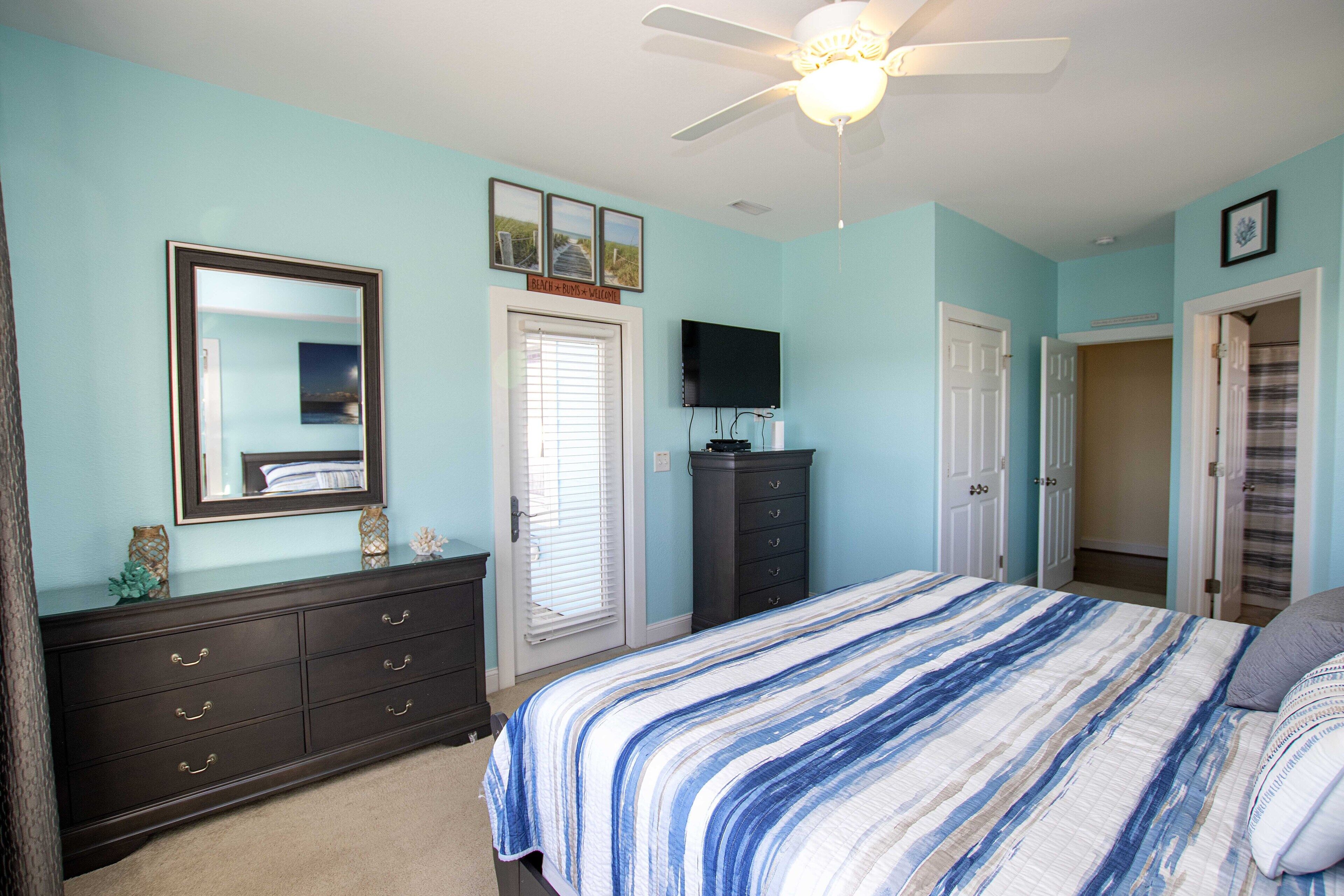 A bedroom with a bed, dresser, television, and a ceiling fan.