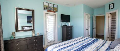 A bedroom with a bed, dresser, television, and a ceiling fan.