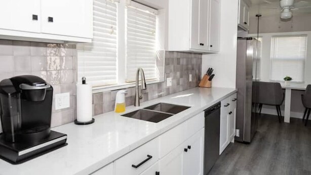 Een moderne keuken met witte kasten, een roestvrijstalen koelkast, een koffiezetapparaat en een gootsteen.