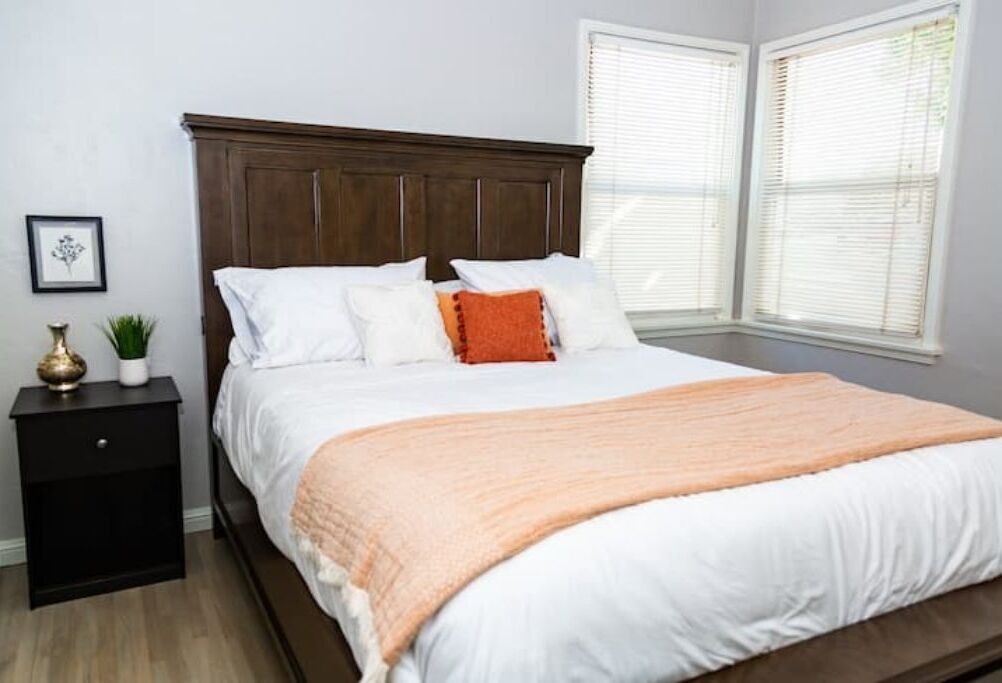 Une chambre avec une tête de lit en bois, du linge de lit blanc et un plaid de couleur pêche.