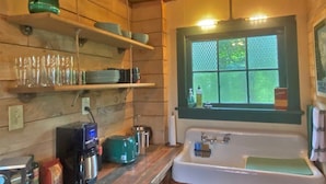 A rustic kitchen with wooden walls, a white sink, and a window with a view of greenery. - Ohana Cabin | WiFi, Wood Stove, AC, Hot tub (Packwood)