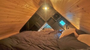 A cozy attic bedroom with a sloped ceiling, a bed, a heater, and a small window. - Ohana Cabin | WiFi, Wood Stove, AC, Hot tub (Packwood)